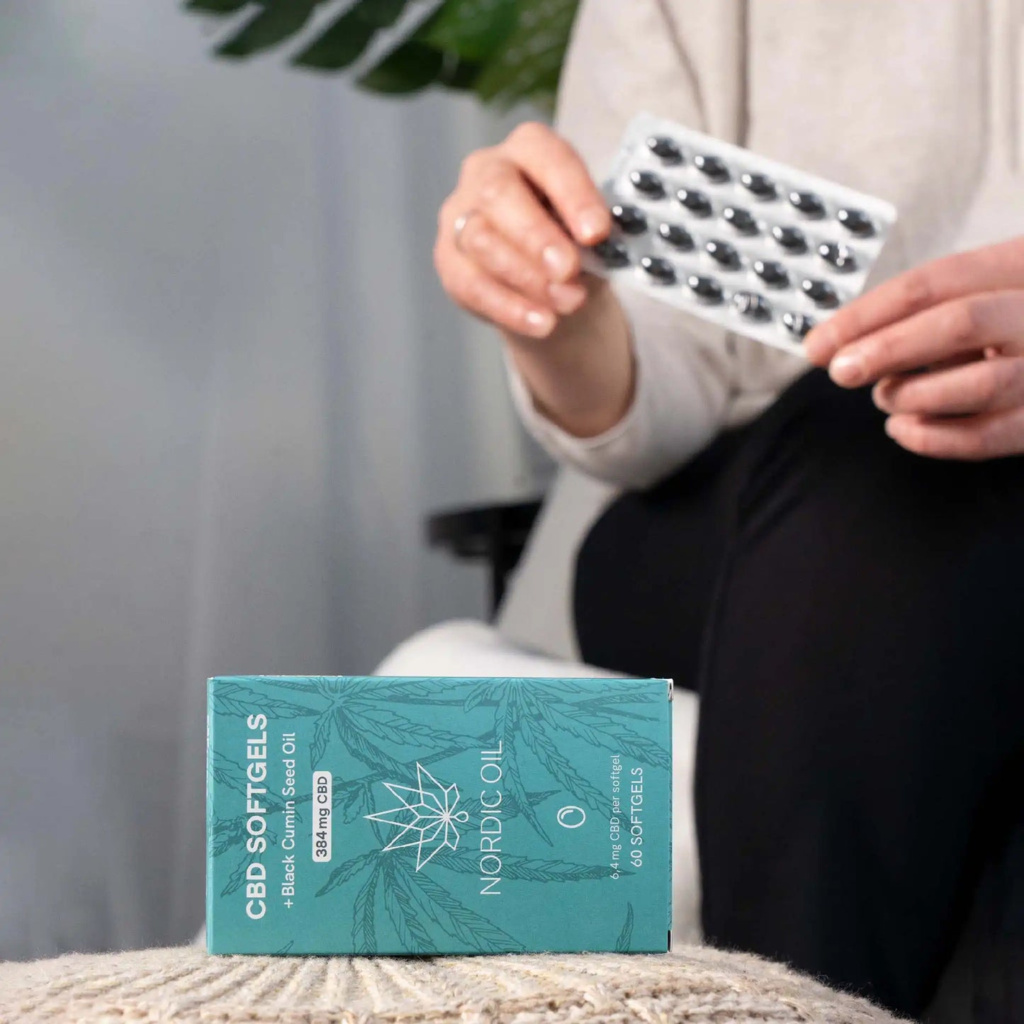 Embalagem de softgels em primeiro plano e cliente segurando softgels em segundo plano