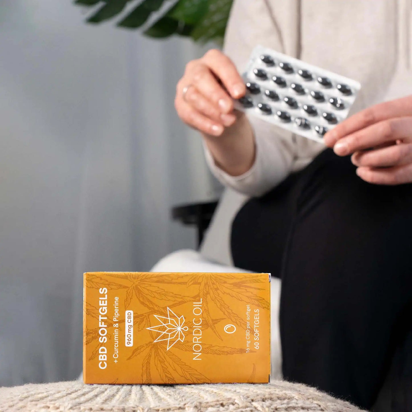 Embalagem de softgels em primeiro plano e cliente segurando softgels em segundo plano